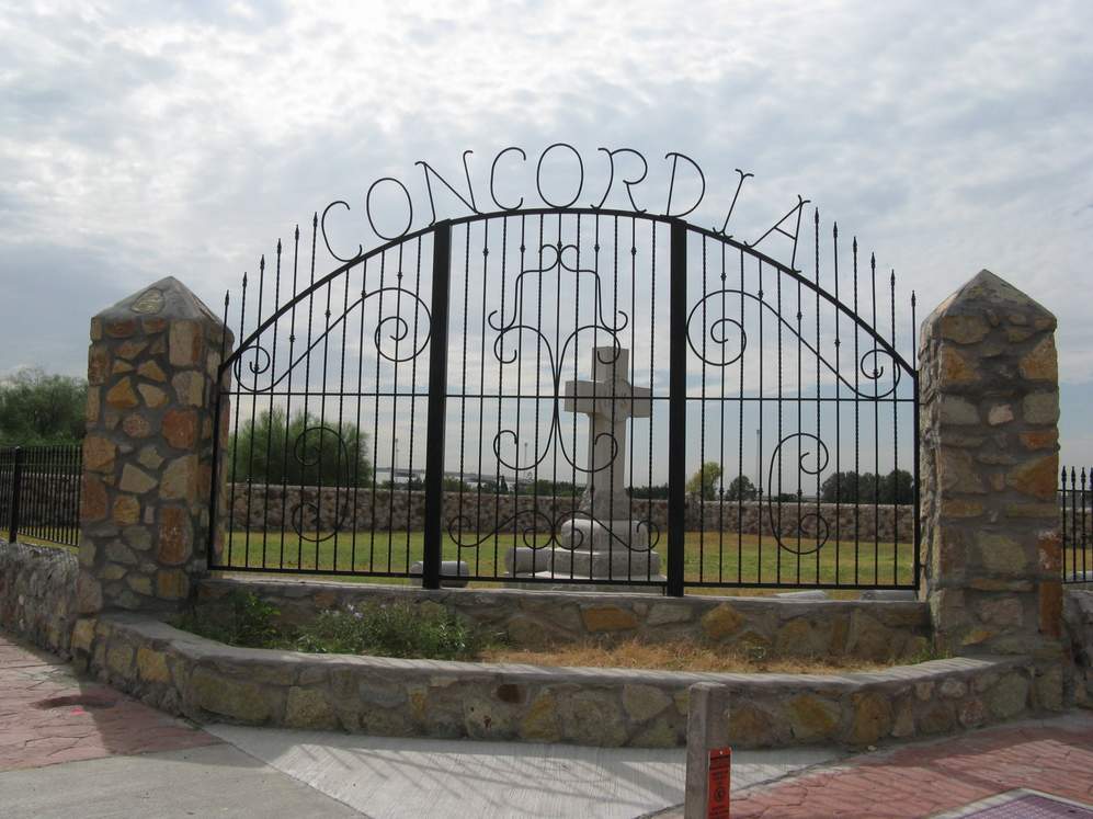 Entrance gate of Concordia Cemetery in El Paso, Texas, featuring ironwork and historic gravestones in the background.