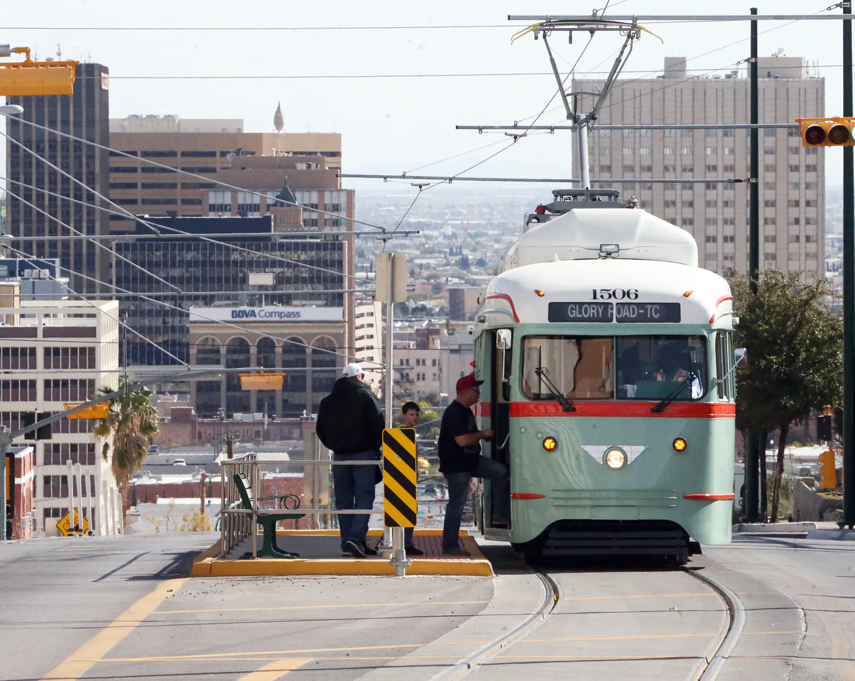 Vintage streetcar in downtown El Paso with passengers boarding, surrounded by historic and modern buildings.