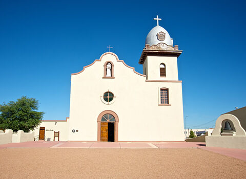 Front view of the historic Ysleta Mission in El Paso, Texas, with its adobe-style façade and blue sky background.