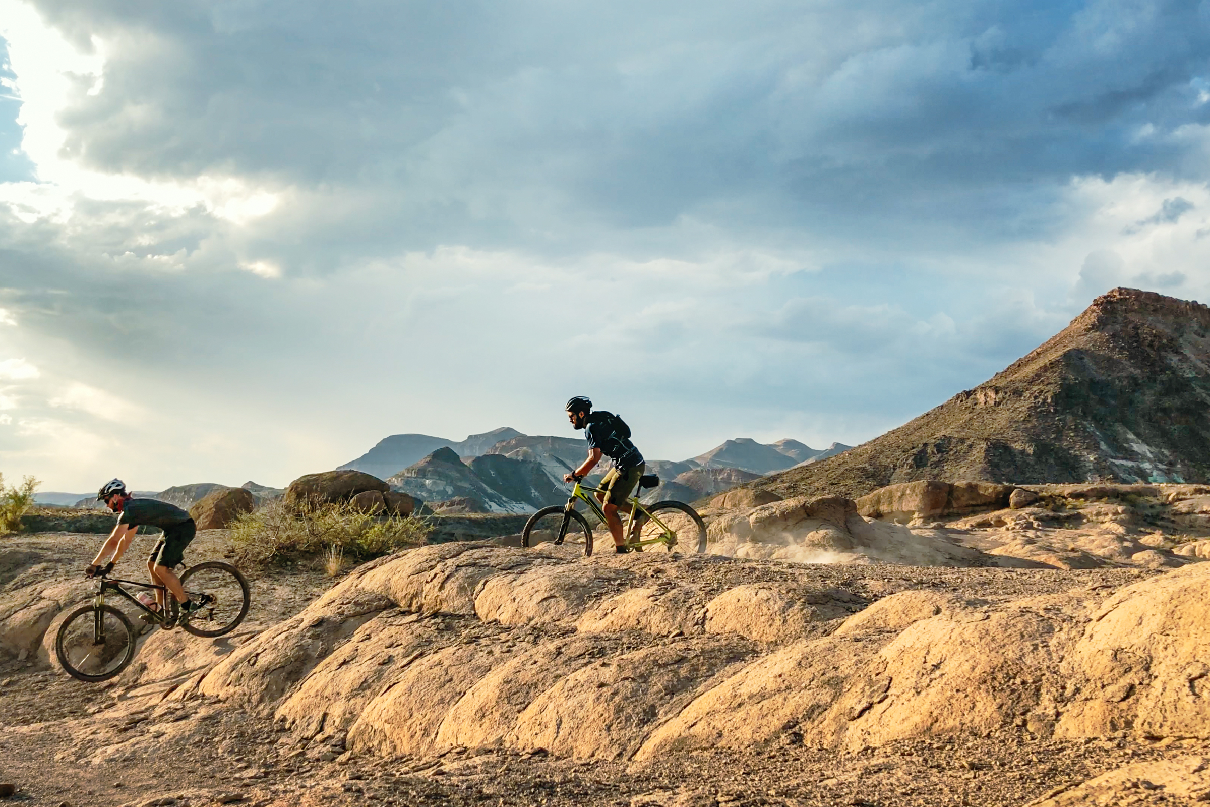 Two cyclists riding across rocky desert trails with mountains in the background at Big Bend Ranch State Park.