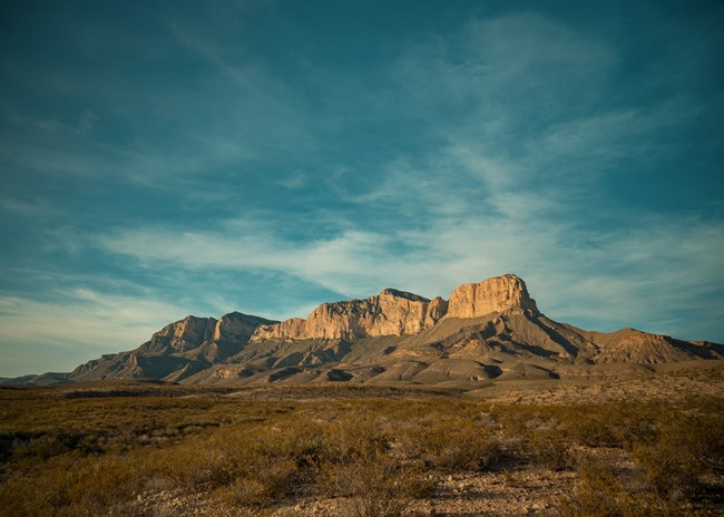 Rocky mountain range under a partly cloudy blue sky in Guadalupe Mountains National Park.