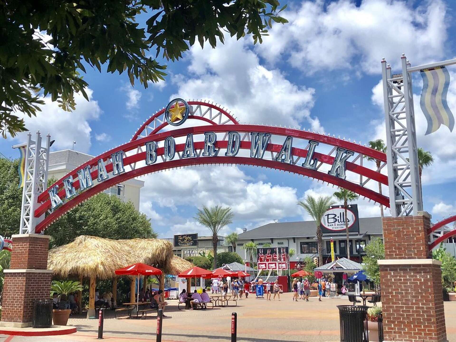 Entrance arch to Kemah Boardwalk with people walking below and palm trees around