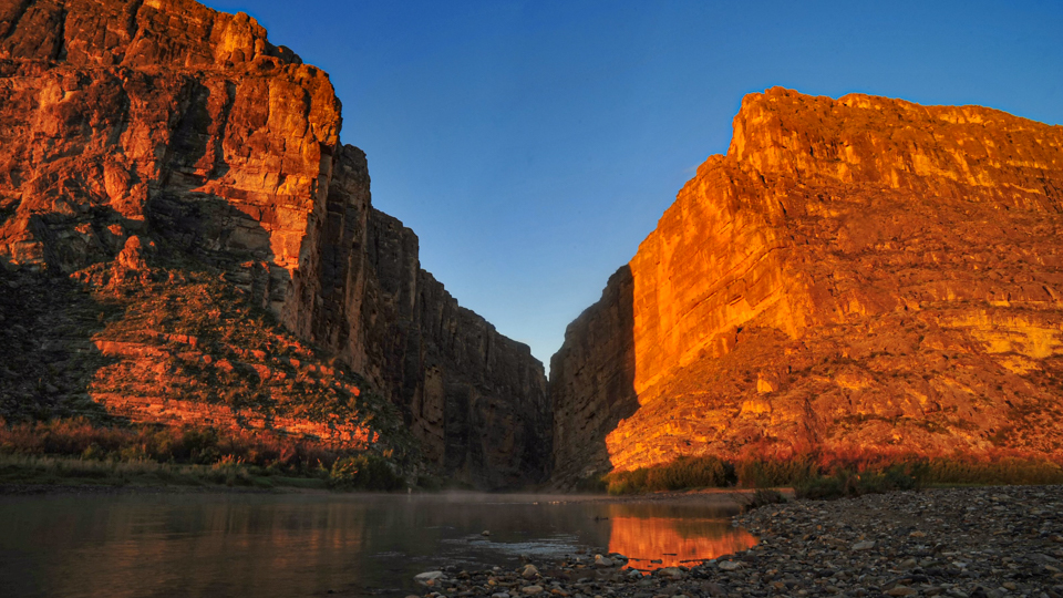 Steep canyon walls glowing orange at sunset with the Rio Grande flowing between them in Big Bend National Park.