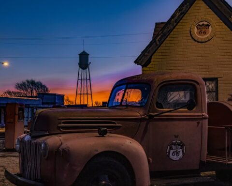 Old truck with Phillips 66 logo parked in Amarillo’s Route 66 District at sunset with a water tower in the background.