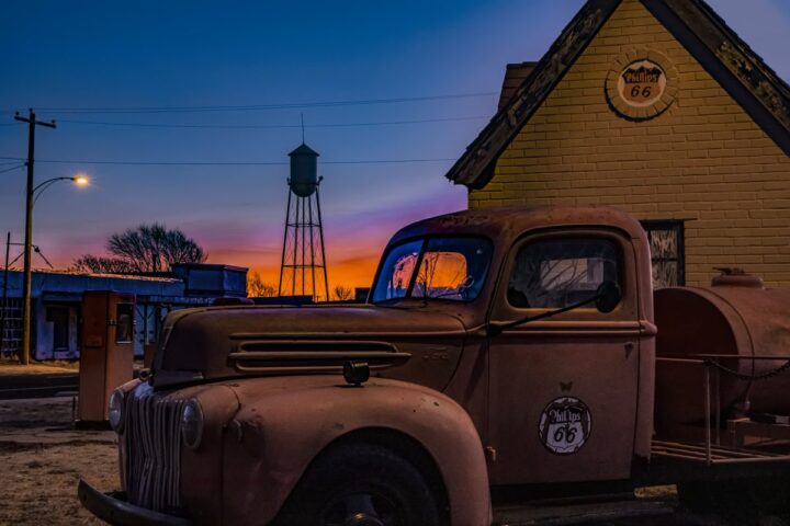 Old truck with Phillips 66 logo parked in Amarillo’s Route 66 District at sunset with a water tower in the background.