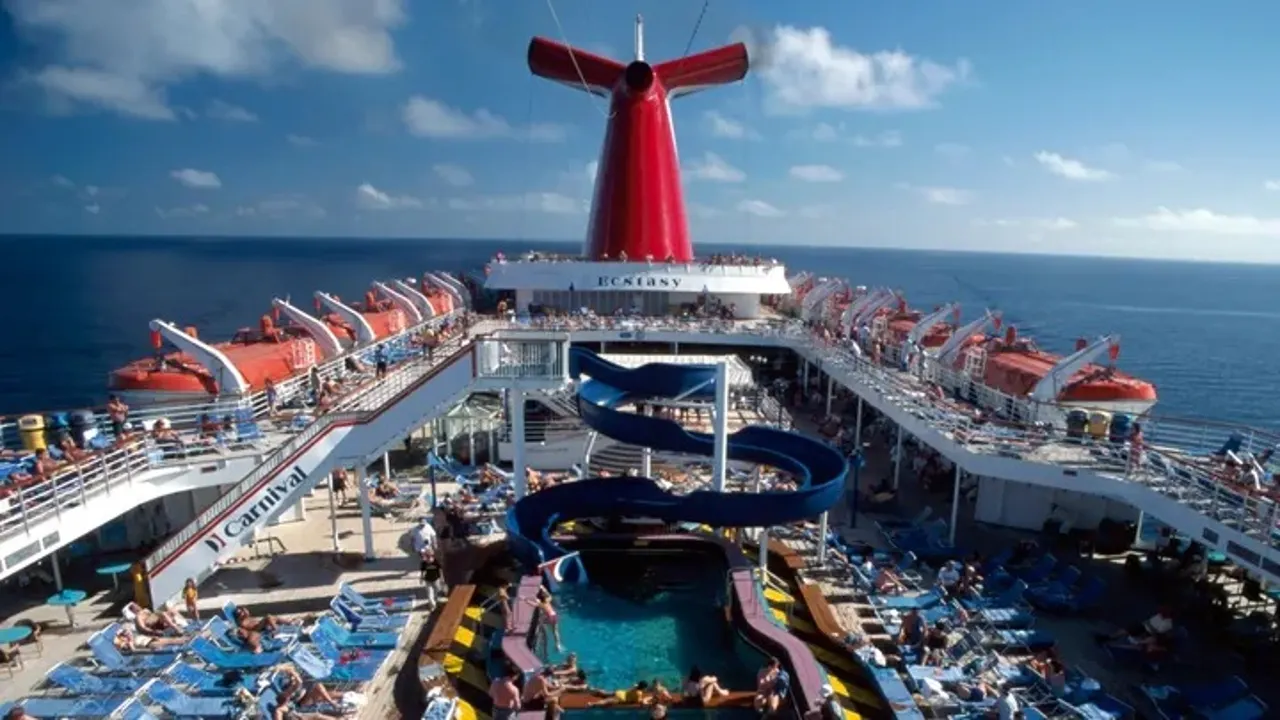 Carnival Cruise Line ship with passengers relaxing by the pool and waterslide at sea.