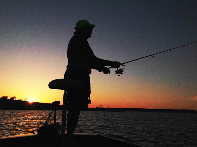 Silhouette of a person fishing from a boat on Lake Amistad during a golden sunset.