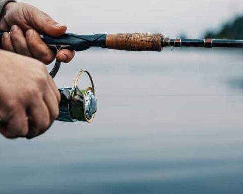 Hands holding a fishing rod and reel over calm waters at Lake Fork in Texas.