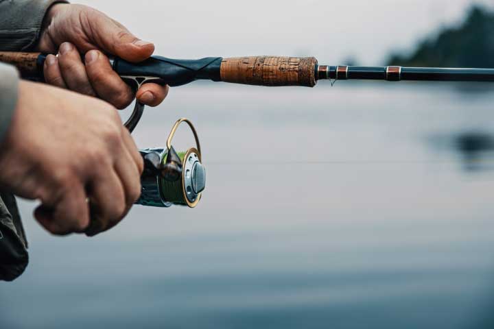 Hands holding a fishing rod and reel over calm waters at Lake Fork in Texas.