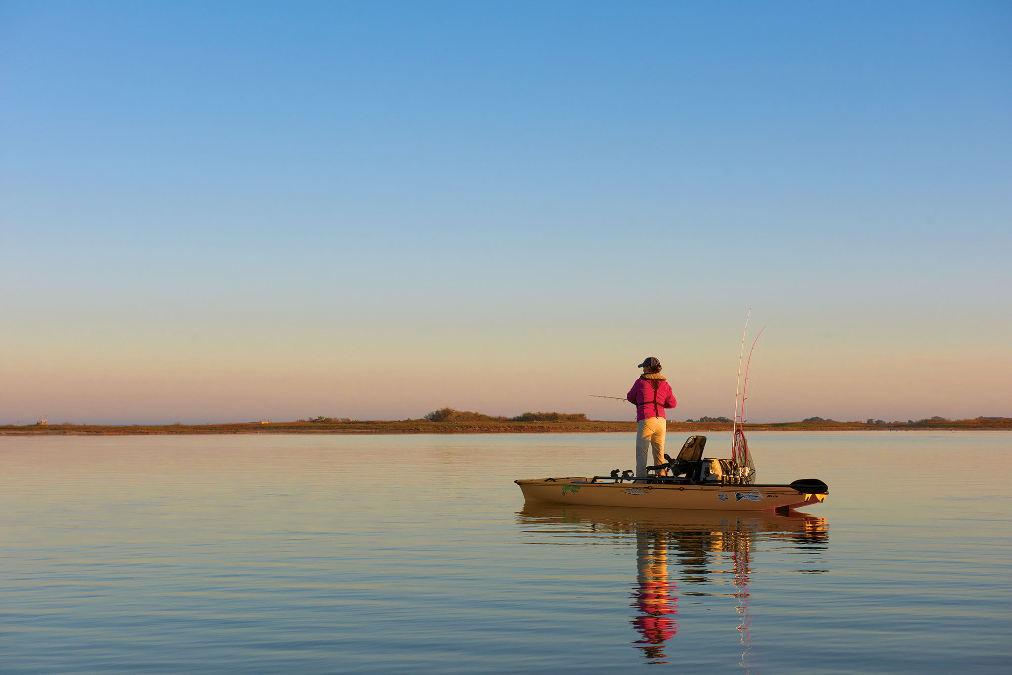 Person fishing from a kayak on the calm waters of Lake LBJ at sunrise, with a clear blue sky in the background.