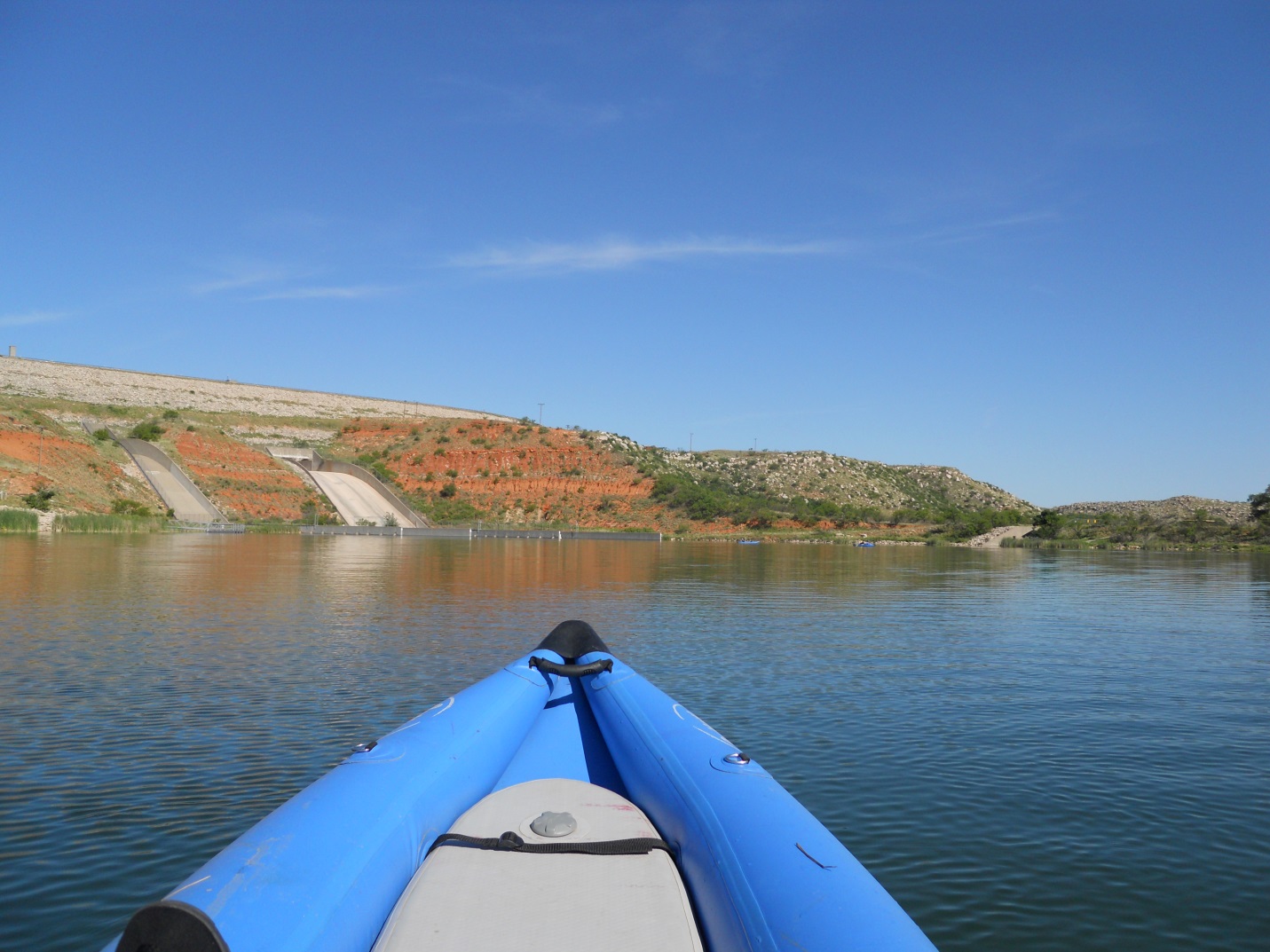 View from a kayak on Lake Meredith, with rocky hills and dam structures under a clear blue sky.