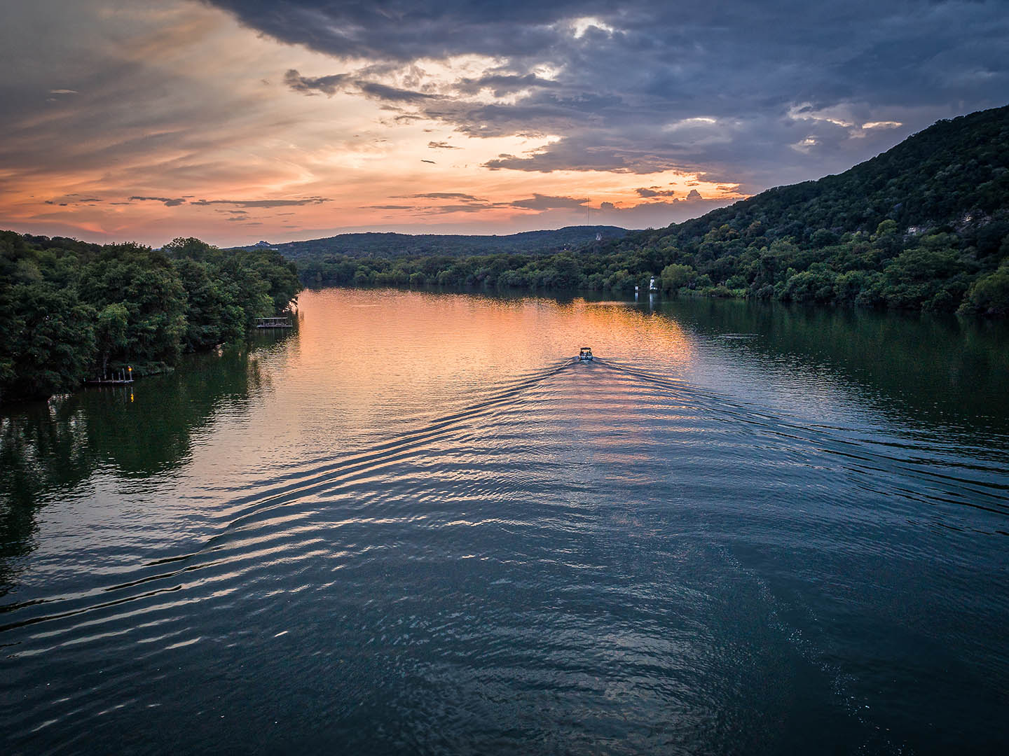 Best Fishing Lakes in Texas: A boat creating ripples on the calm waters of Marble Falls at sunset with surrounding tree-covered hills.