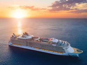 Royal Caribbean International cruise ship sailing at sunset with full view of decks and outdoor activities.