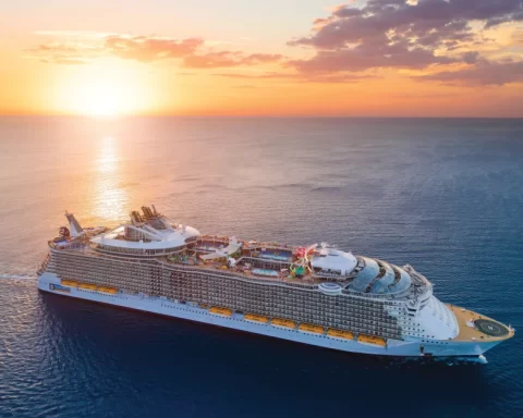 Royal Caribbean International cruise ship sailing at sunset with full view of decks and outdoor activities.