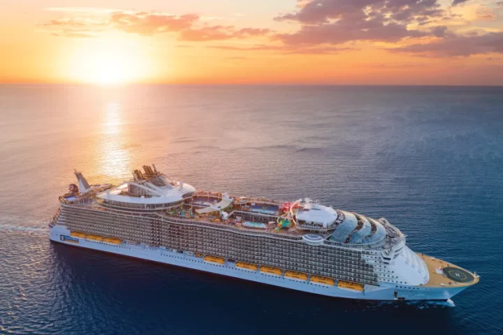 Royal Caribbean International cruise ship sailing at sunset with full view of decks and outdoor activities.