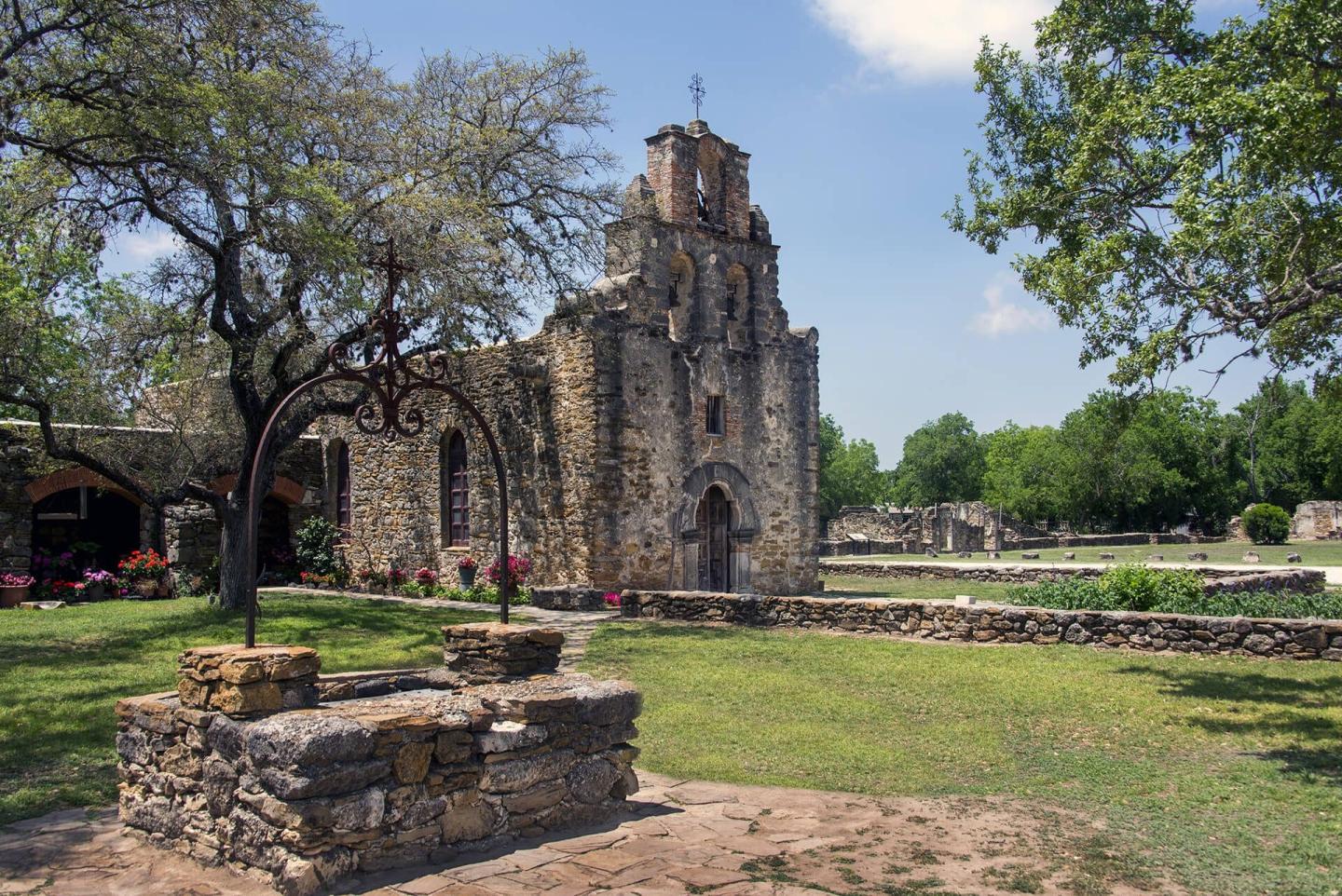 Old stone church surrounded by trees and gardens at San Antonio Missions National Historical Park in Texas.