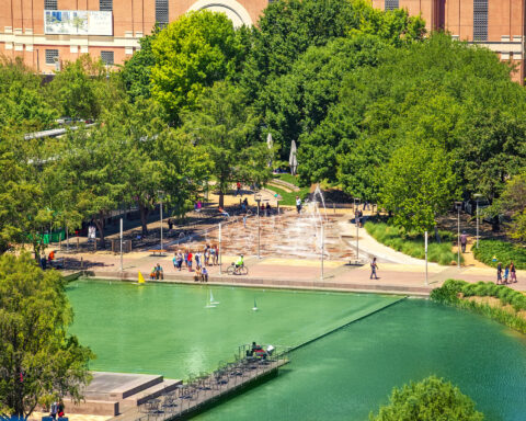 Aerial view of Discovery Green park with fountains, lake, and families walking in downtown Houston.