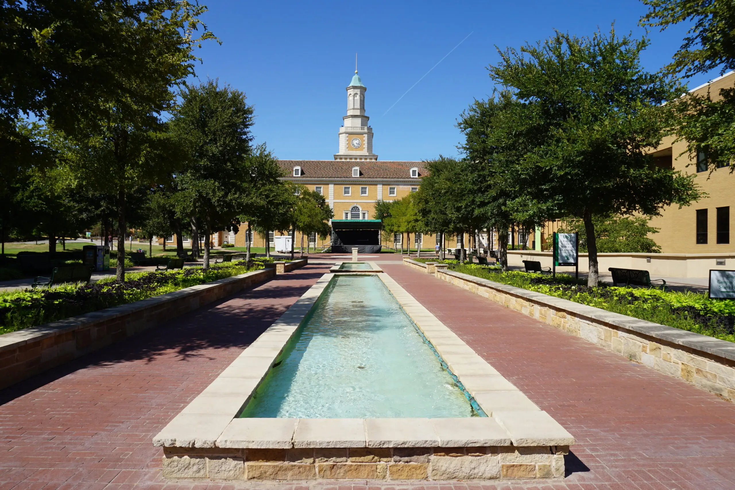 Campus view of the University of North Texas in Denton featuring a fountain and main building under a clear blue sky.