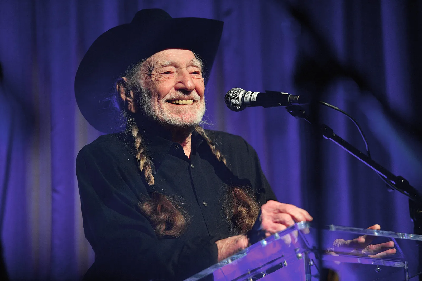 Willie Nelson performing on stage in a cowboy hat and braids in Texas.