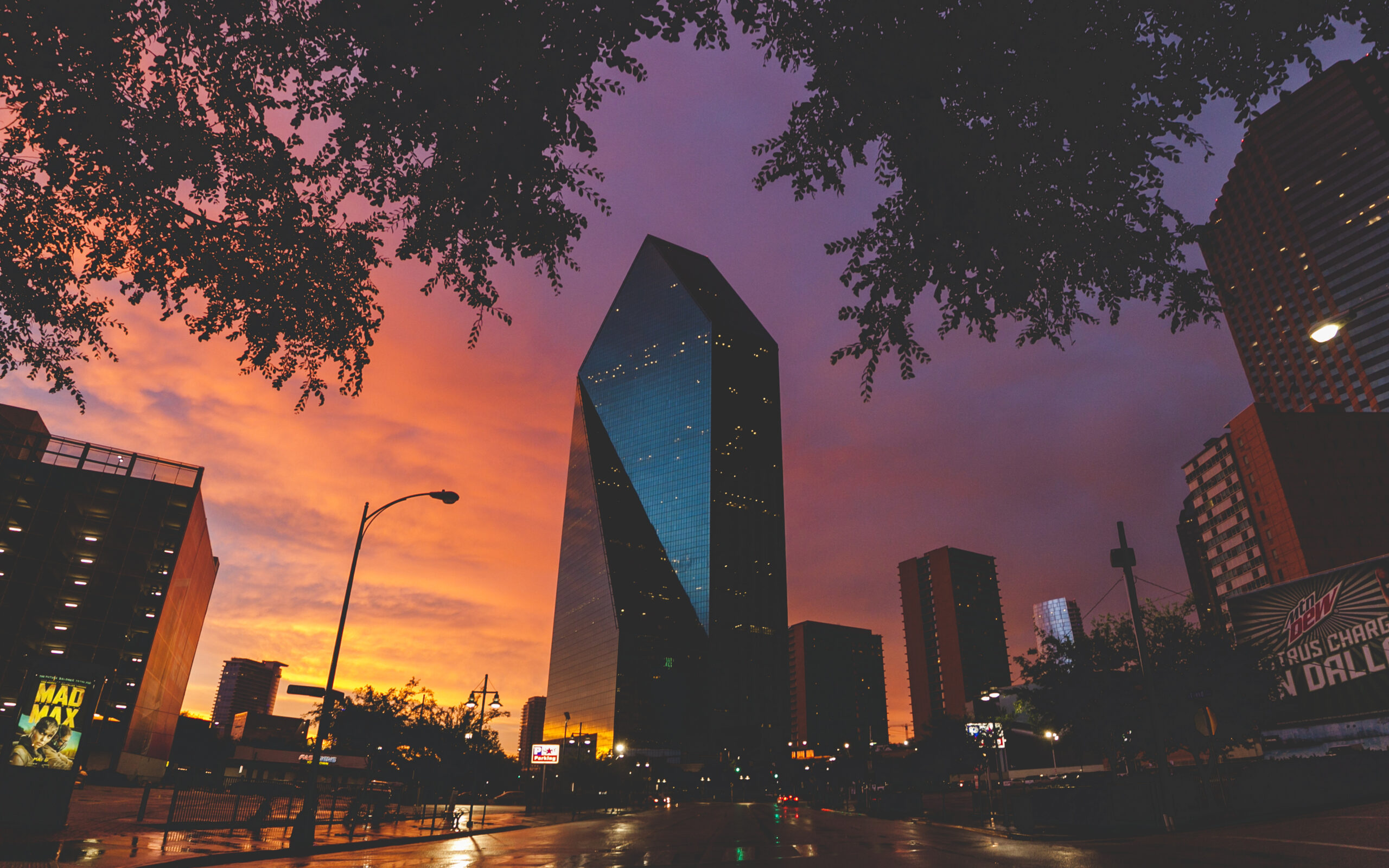 Sunset view of downtown Dallas skyscrapers with a vivid orange and purple sky.