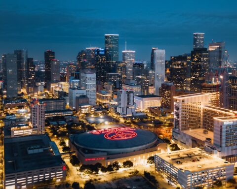 Texas’ Tinseltown - Nighttime aerial view of downtown Houston skyline with illuminated buildings and the Toyota Center in the foreground.