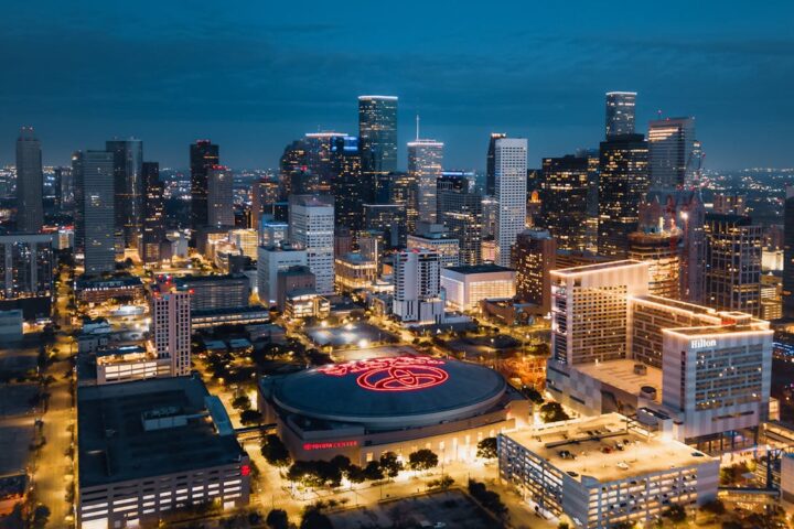 Texas’ Tinseltown - Nighttime aerial view of downtown Houston skyline with illuminated buildings and the Toyota Center in the foreground.