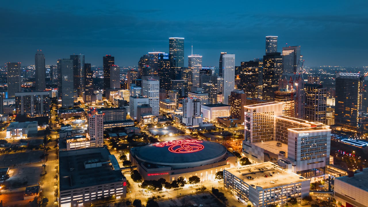 Texas’ Tinseltown - Nighttime aerial view of downtown Houston skyline with illuminated buildings and the Toyota Center in the foreground.