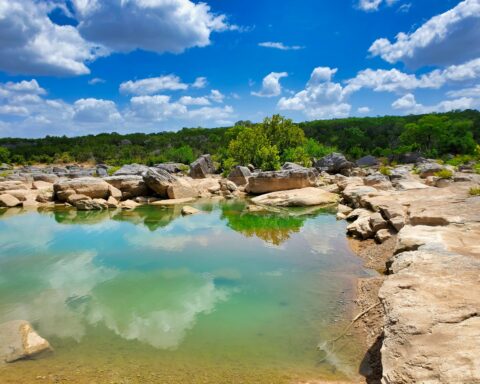 Clear turquoise water surrounded by large rock formations and lush greenery in Subtropical Texas.