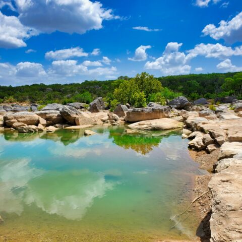 Clear turquoise water surrounded by large rock formations and lush greenery in Subtropical Texas.