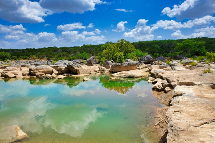 Clear turquoise water surrounded by large rock formations and lush greenery in Subtropical Texas.