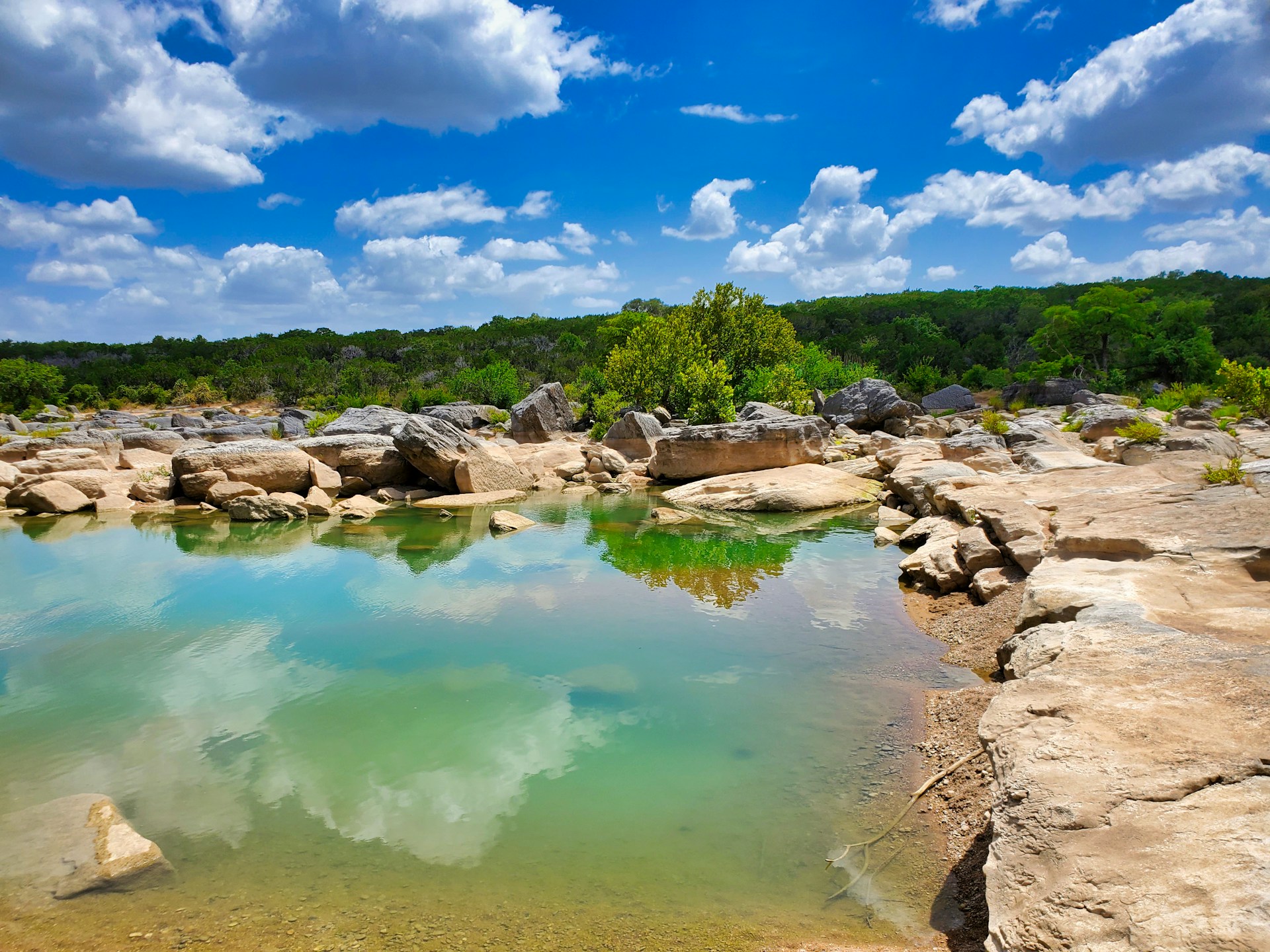 Clear turquoise water surrounded by large rock formations and lush greenery in Subtropical Texas.