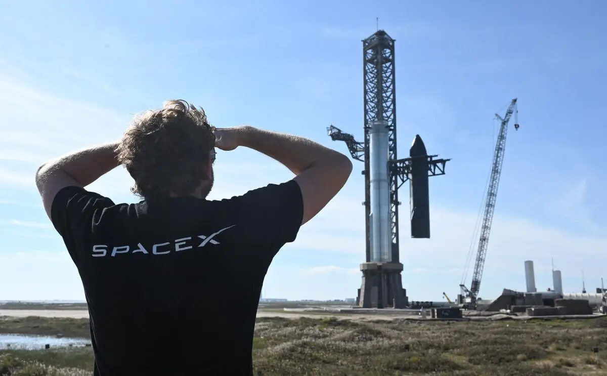 Person wearing a SpaceX shirt looking at the Starship launch tower at SpaceX Starbase, capturing what it’s like to visit Starbase.